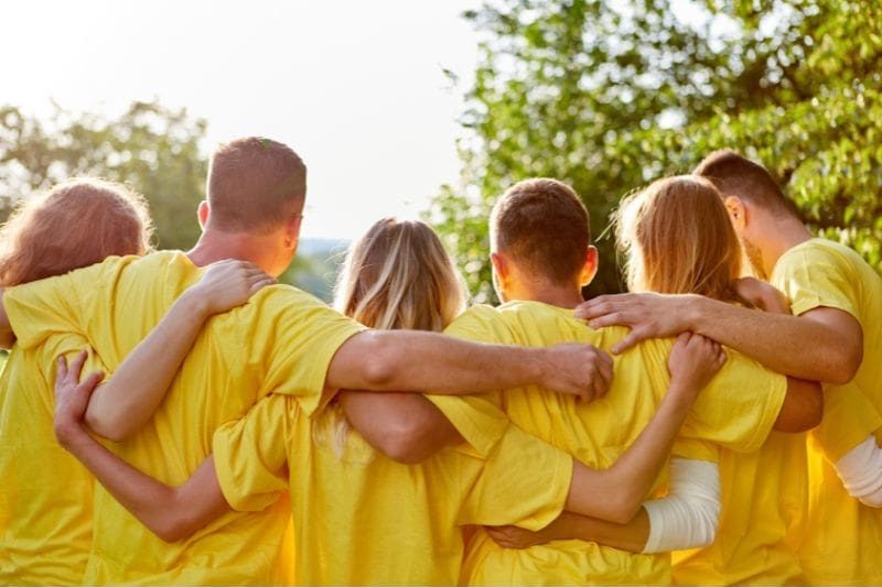 A group of people in yellow shirts stands together outdoors, their arms around each other, embodying team empowerment.
