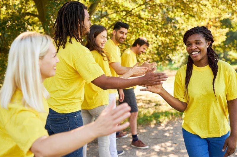 A group of people in yellow shirts is outdoors, surrounded by trees, high-fiving each other in a celebration of team empowerment and leadership.