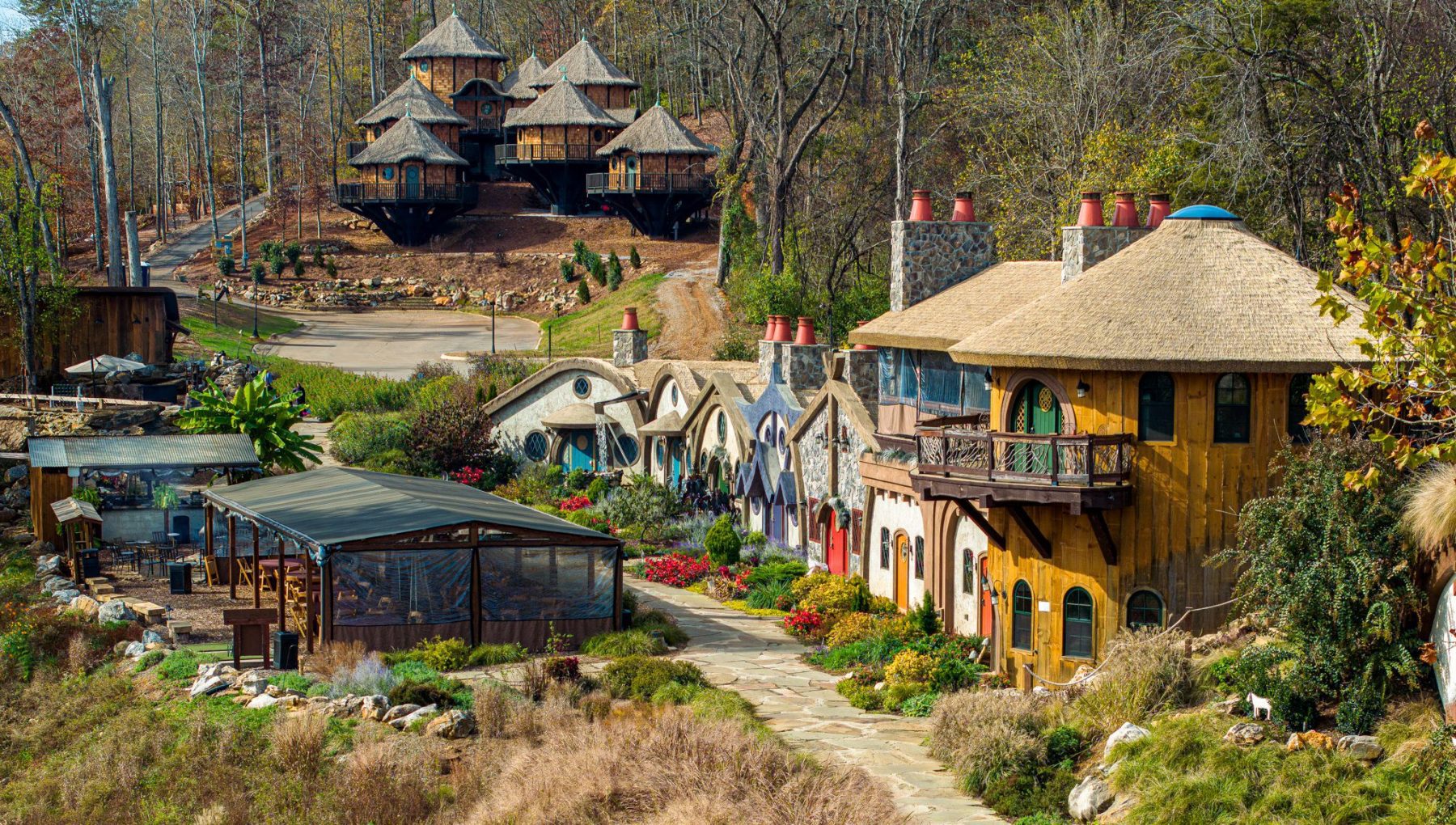 Fairytale village with whimsical houses, lush gardens, and forest backdrop under a clear sky.