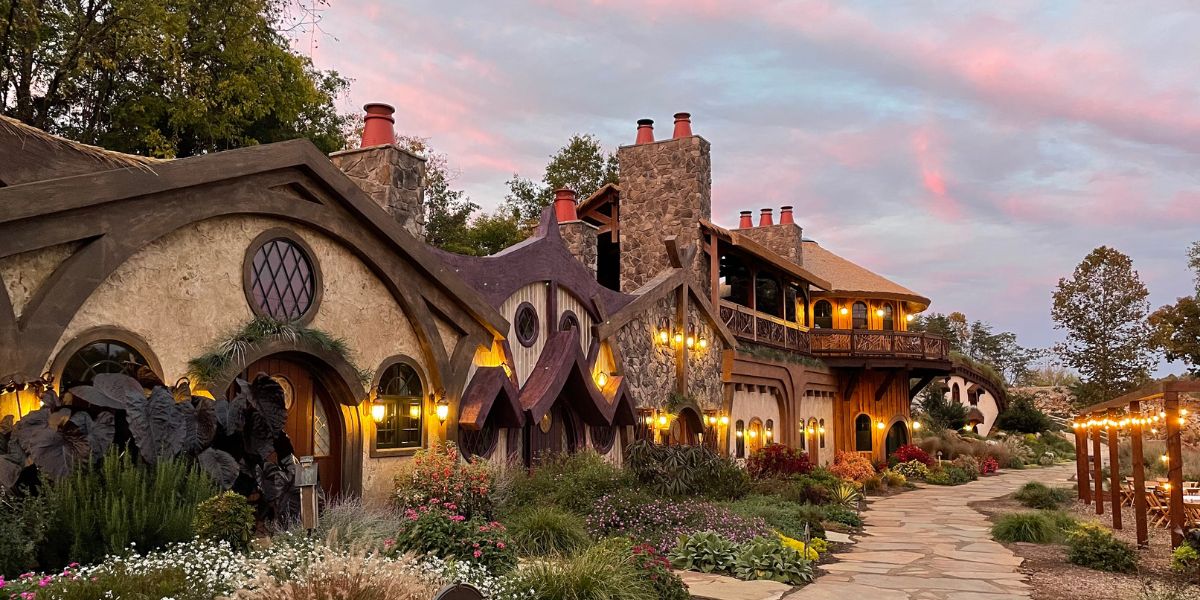 A whimsical, cottage-style house with rounded doors, lanterns, and lush garden at sunset, resembling a fairy tale setting.