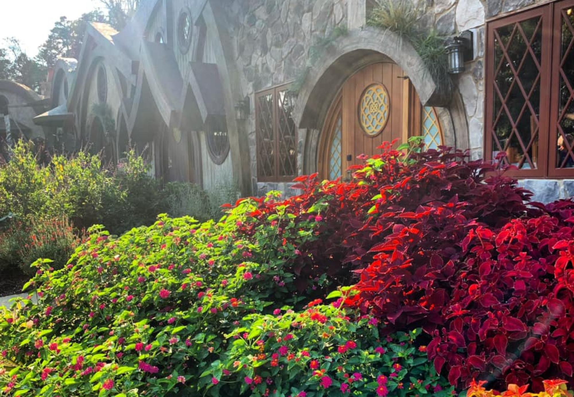A scenic view of a house with round doors and lush green, red, and pink foliage in the foreground.